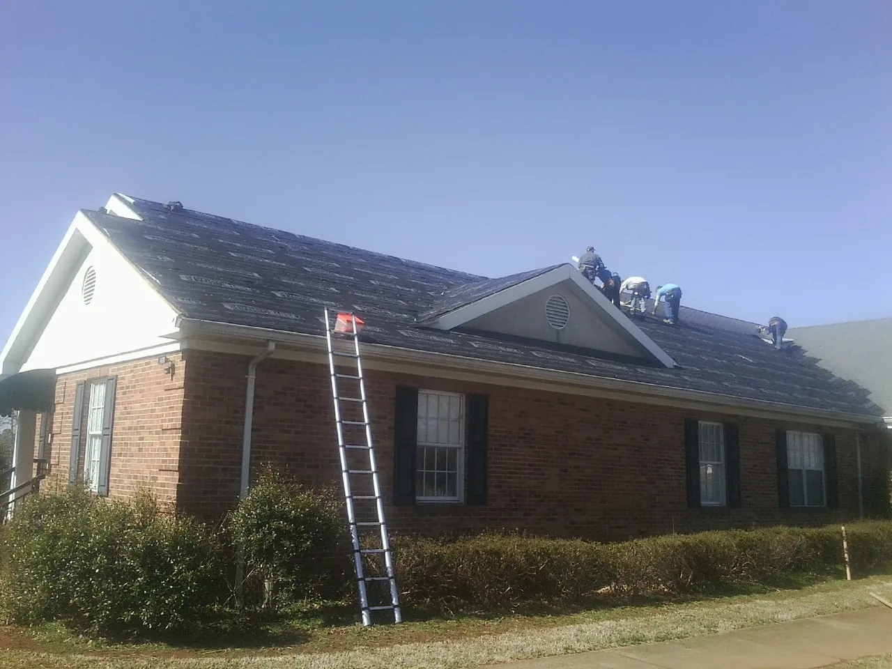 Crew tearing shingles off a brick ranch roof with a ladder set — Emergency Roof Repair work by our crew in Moss Point