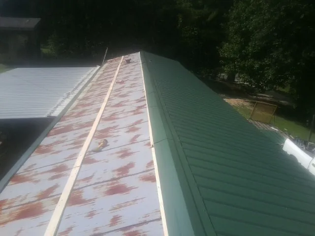 Old rusted panels beside newly installed green metal roofing — Wind Damage Roof Repair by Roofing Brothers in Moss Point