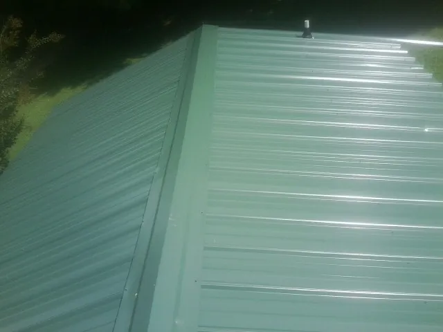 New green metal panels meeting at the ridge of a roof — Flat Roof Repair work by our crew in Moss Point