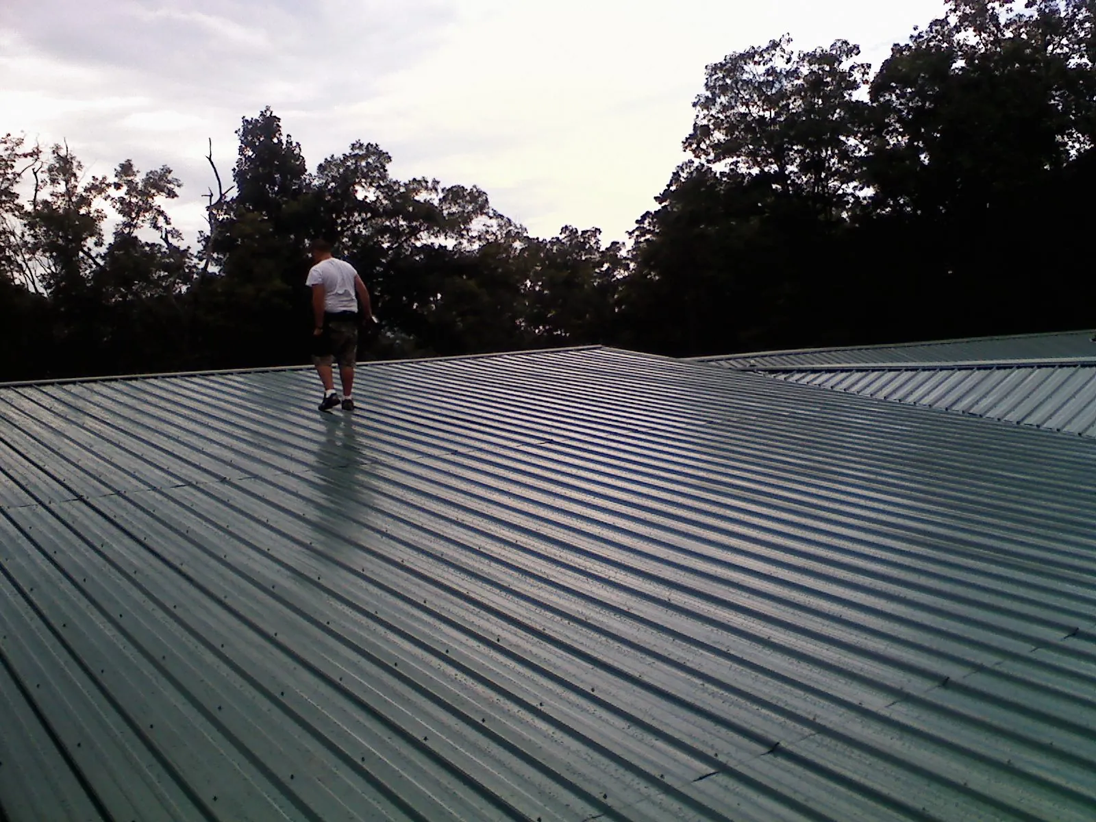 Roofer walking a wide expanse of new green metal roofing in Moss Point