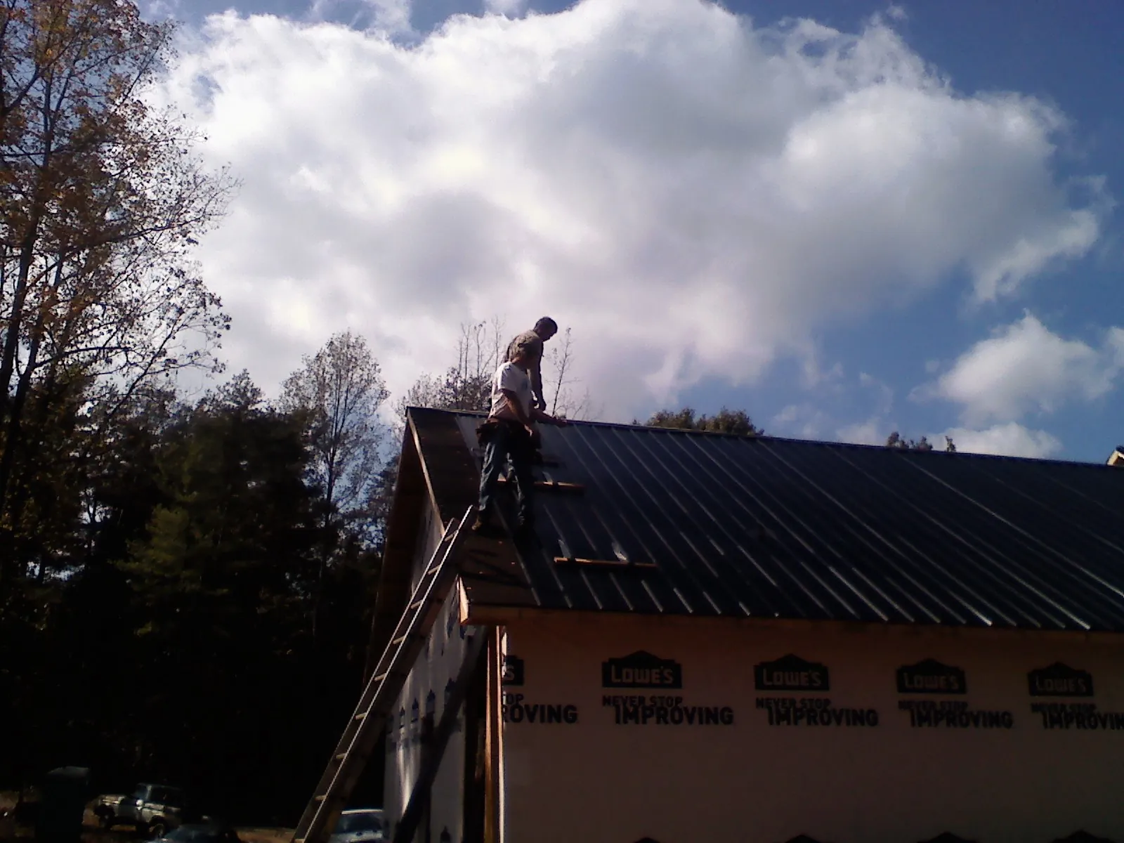 Roofer fastening dark metal panels high against a cloudy sky, from a Roof Inspection job in Moss Point