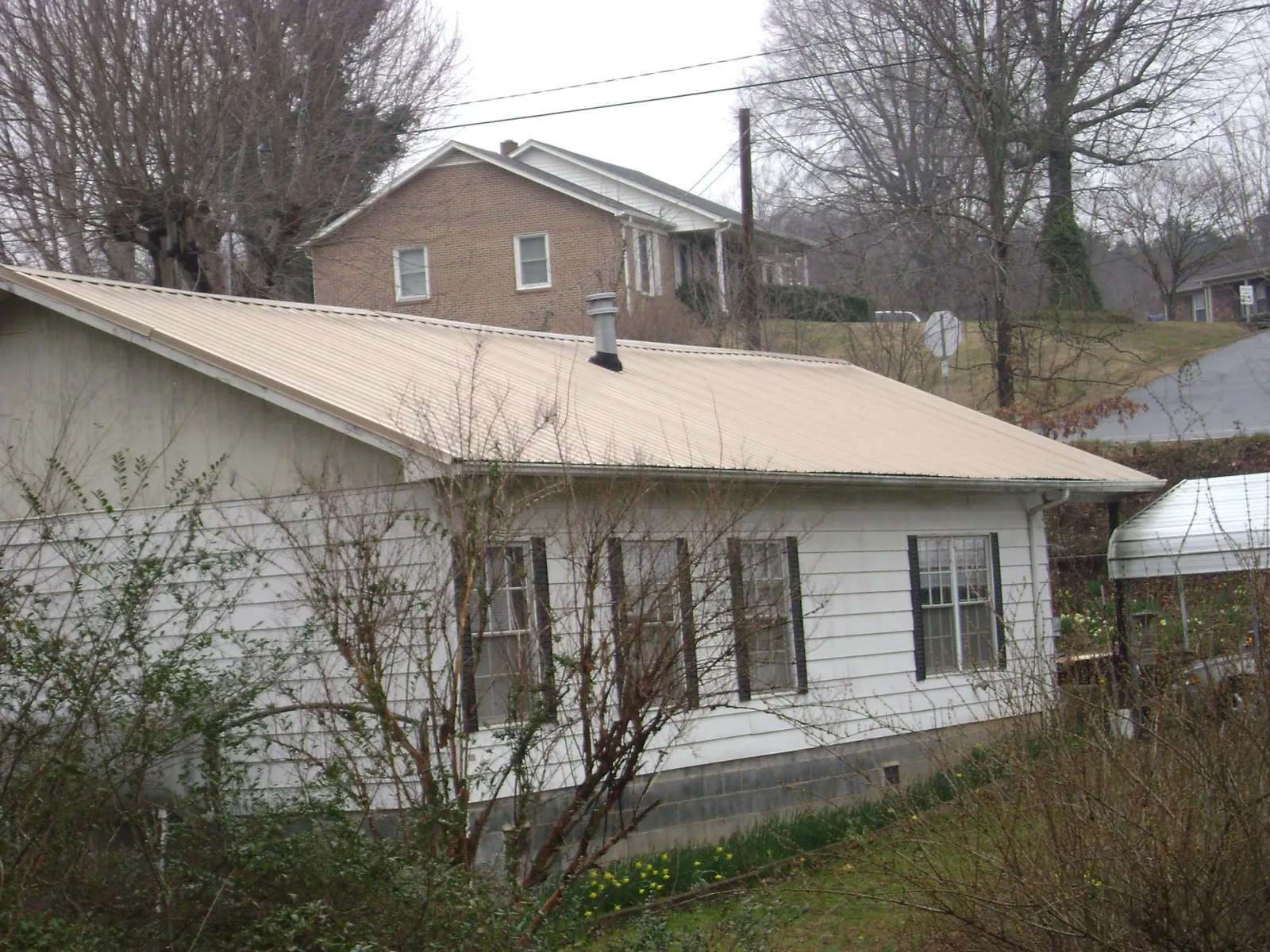 Tan metal roof on a white sided house set into a hillside — Commercial Roofing by Roofing Brothers in Moss Point