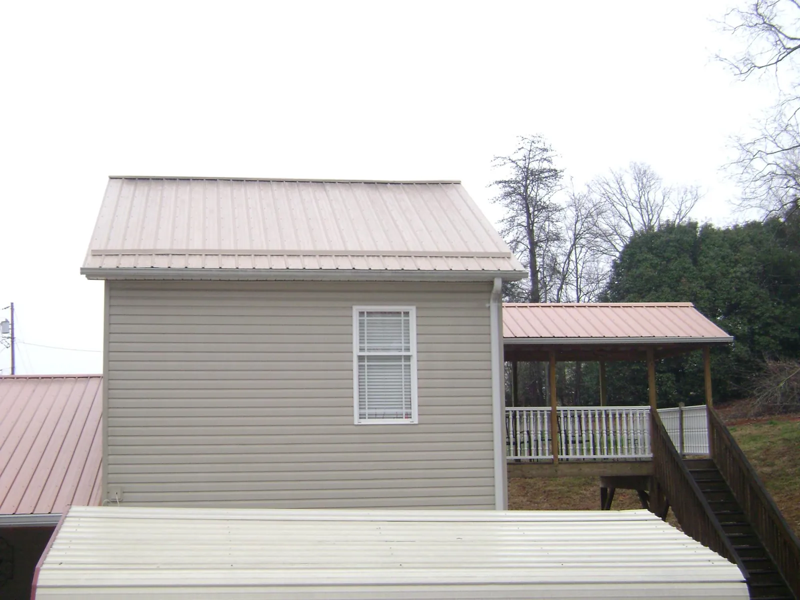 Tan metal roofs on a two story addition and attached porch, from a Roof Replacement job in Moss Point